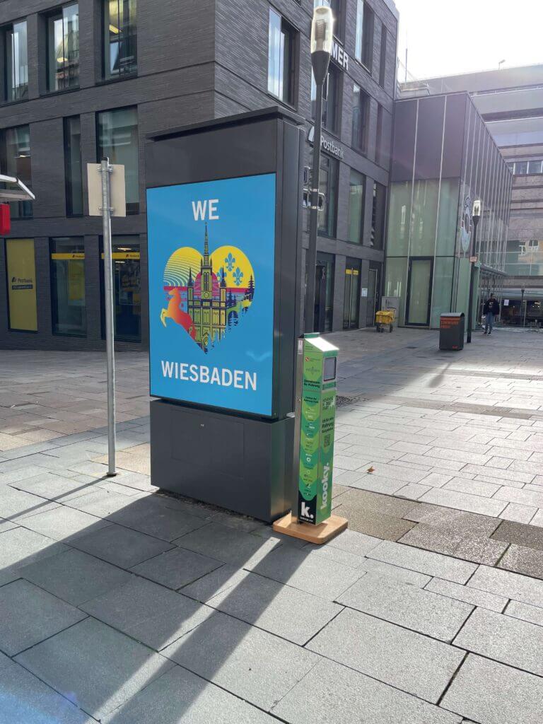 Ein kooky Automat steht an einem Werbeschild mit der Aufschrift: We love Wiesbaden.